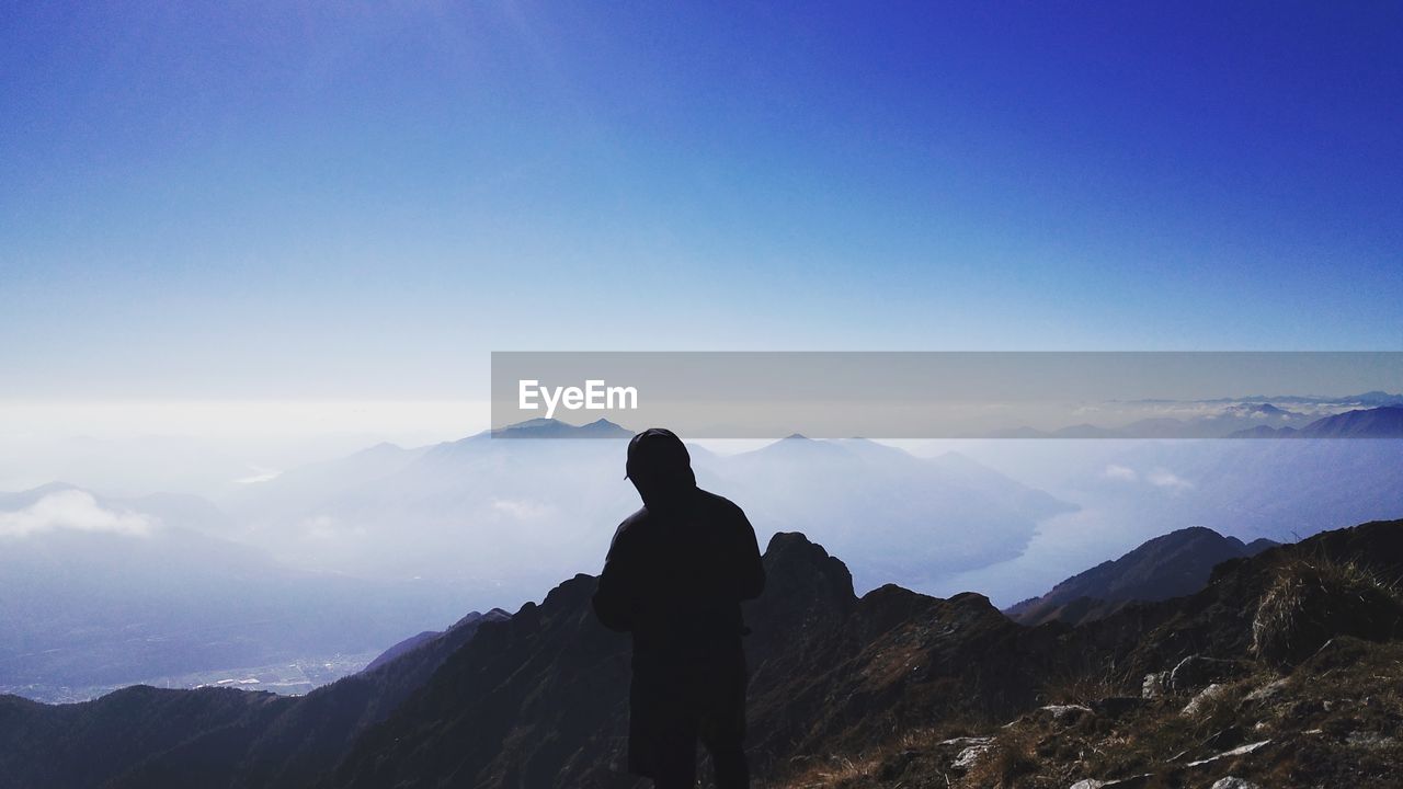 REAR VIEW OF SILHOUETTE MAN STANDING ON MOUNTAIN