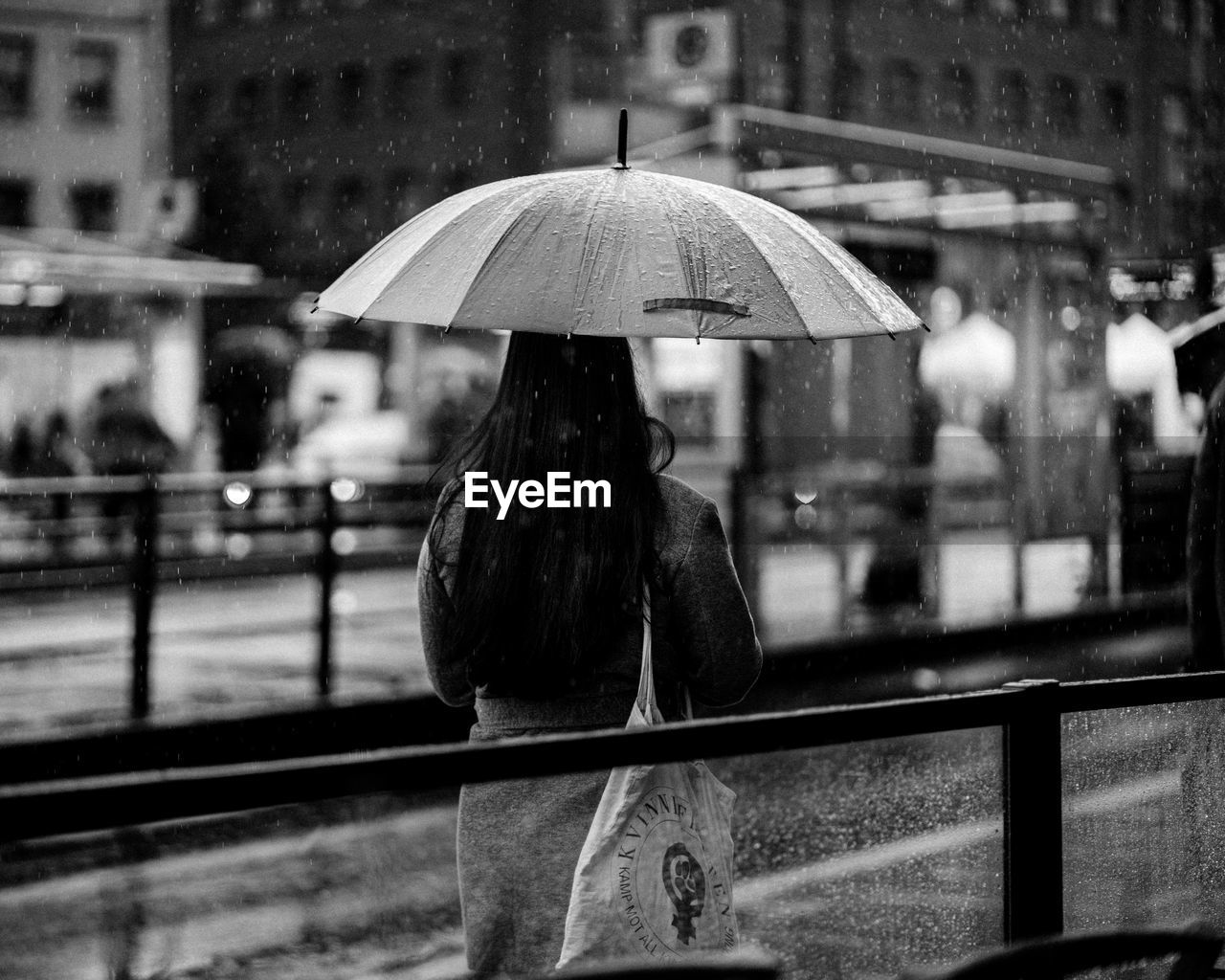 REAR VIEW OF WOMAN STANDING ON WET RAILING DURING RAINY SEASON