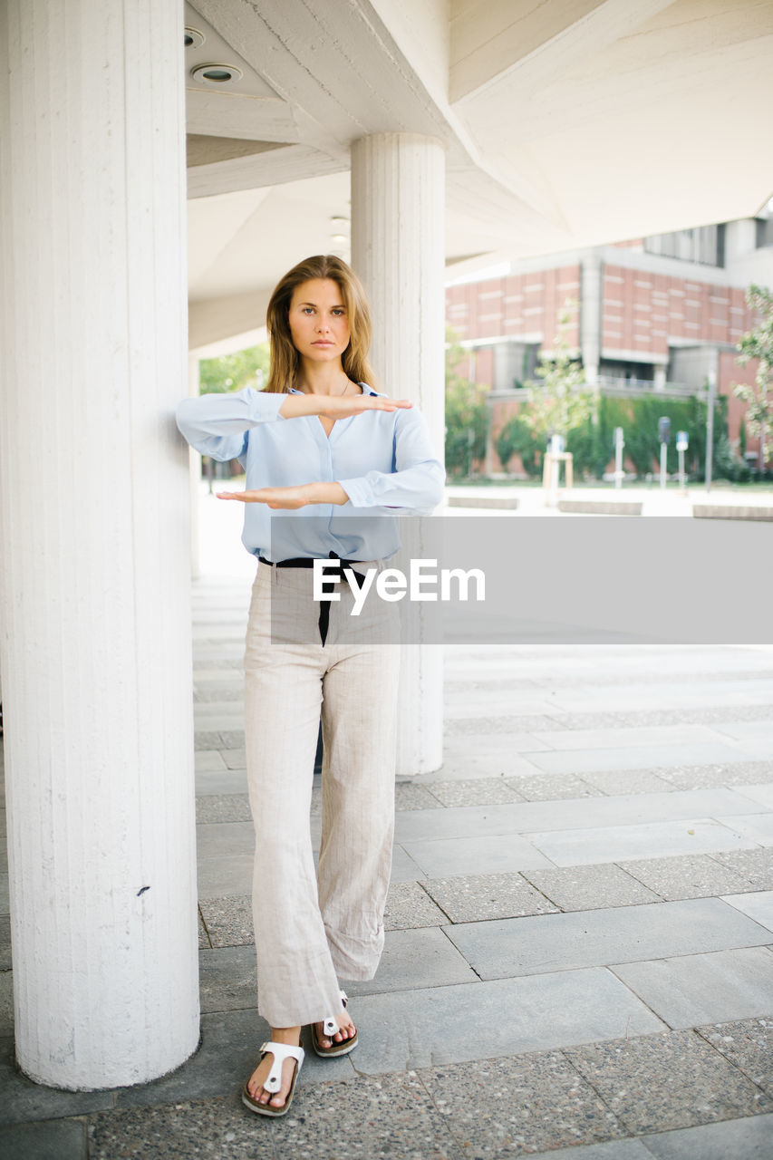 Portrait of young woman gesturing equal sign while standing by column