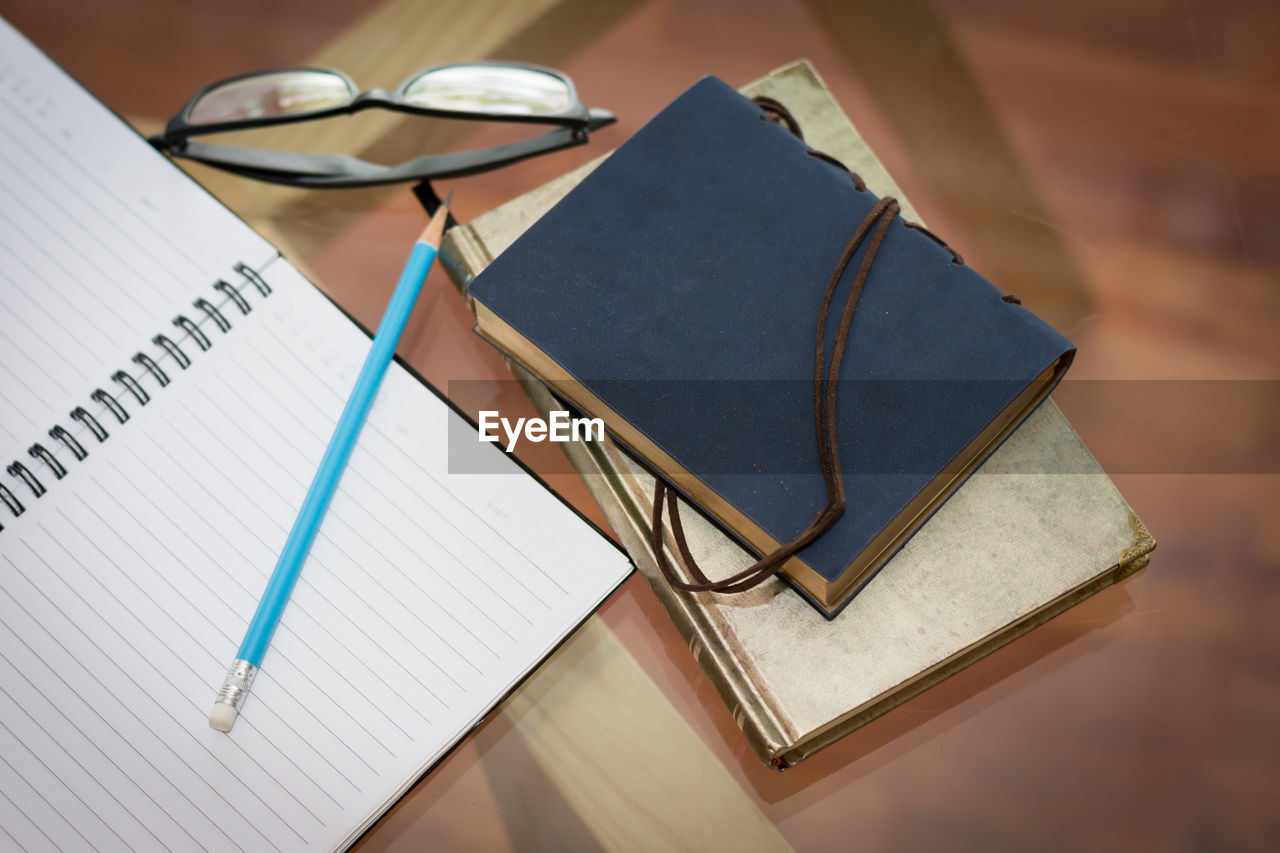 High angle view of books with eyeglasses and pencil on table