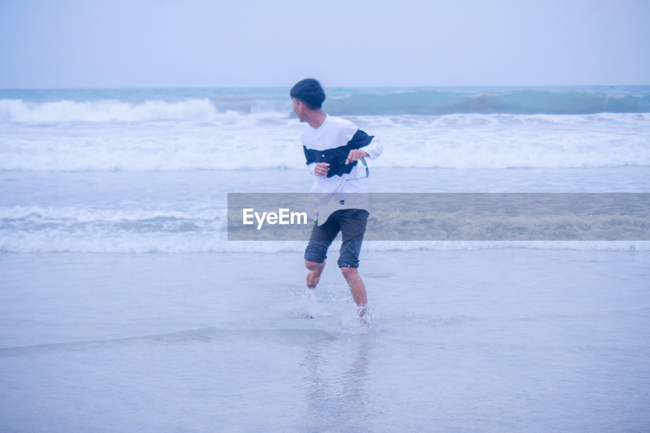 Playful young man standing on shore at beach