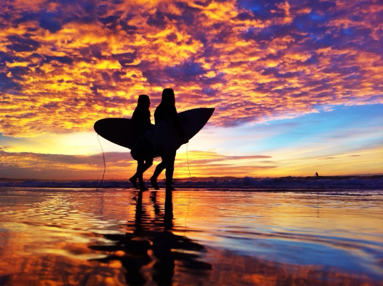 Two silhouette men with surfboards on beach at sunset
