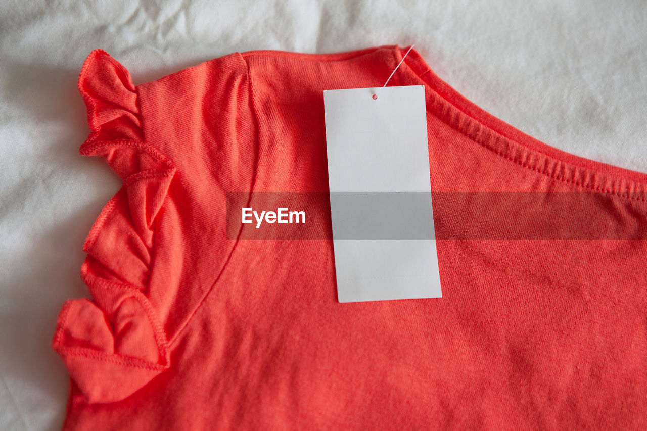 Directly above shot of red t-shirt with blank price tag over bed
