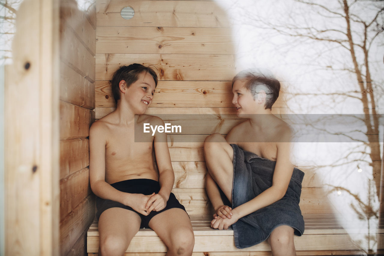 Smiling shirtless boys talking with each other while sitting in sauna