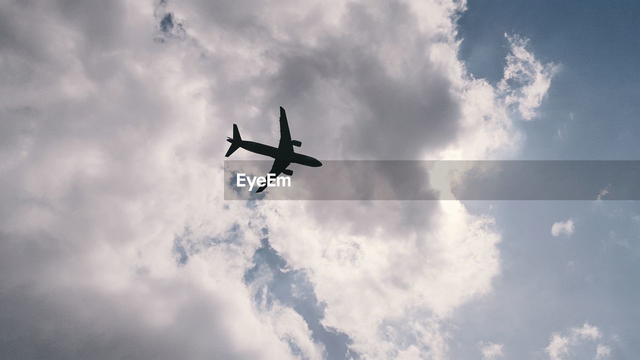 Low angle view of airplane flying against cloudy sky