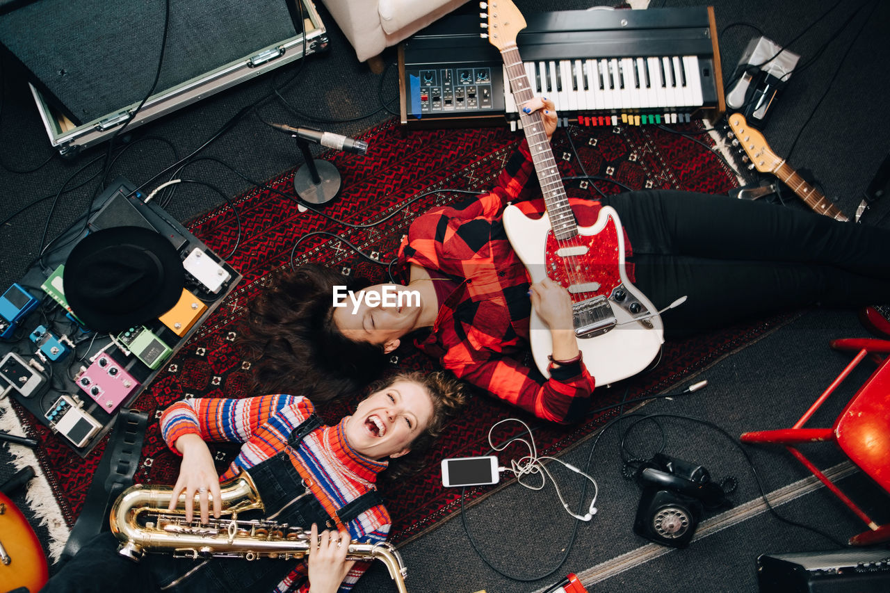 High angle view of happy female musicians playing instruments while lying on carpet