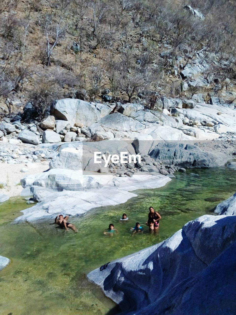 GROUP OF PEOPLE ON ROCK BY SNOW COVERED ROCKS