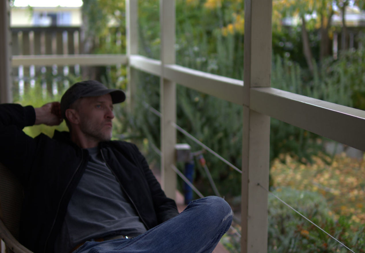 one person, adult, sitting, men, person, hat, three quarter length, casual clothing, sadness, architecture, contemplation, clothing, lifestyles, looking, relaxation, human face, social issues, day, beard, outdoors, depression - sadness, leisure activity, facial hair, nature, loneliness, railing, mature adult, fence, focus on foreground, plant, looking away, solitude, cap, emotion, side view