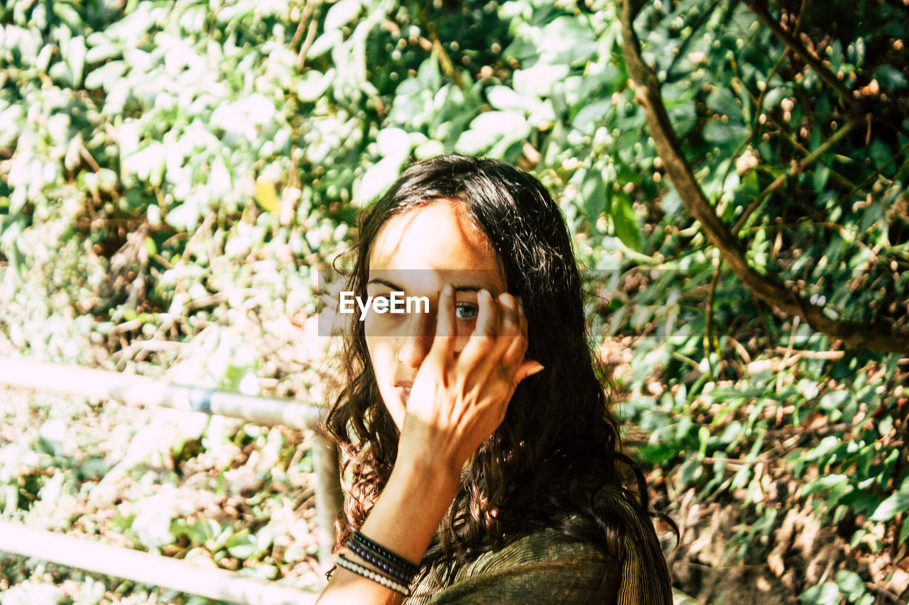 PORTRAIT OF YOUNG WOMAN IN FOREST AGAINST TREES