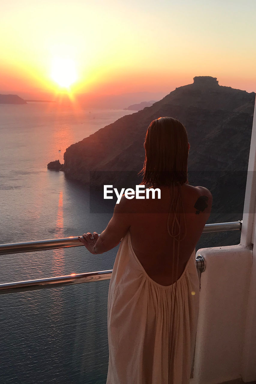 Rear view of woman looking at sea against sky during sunset