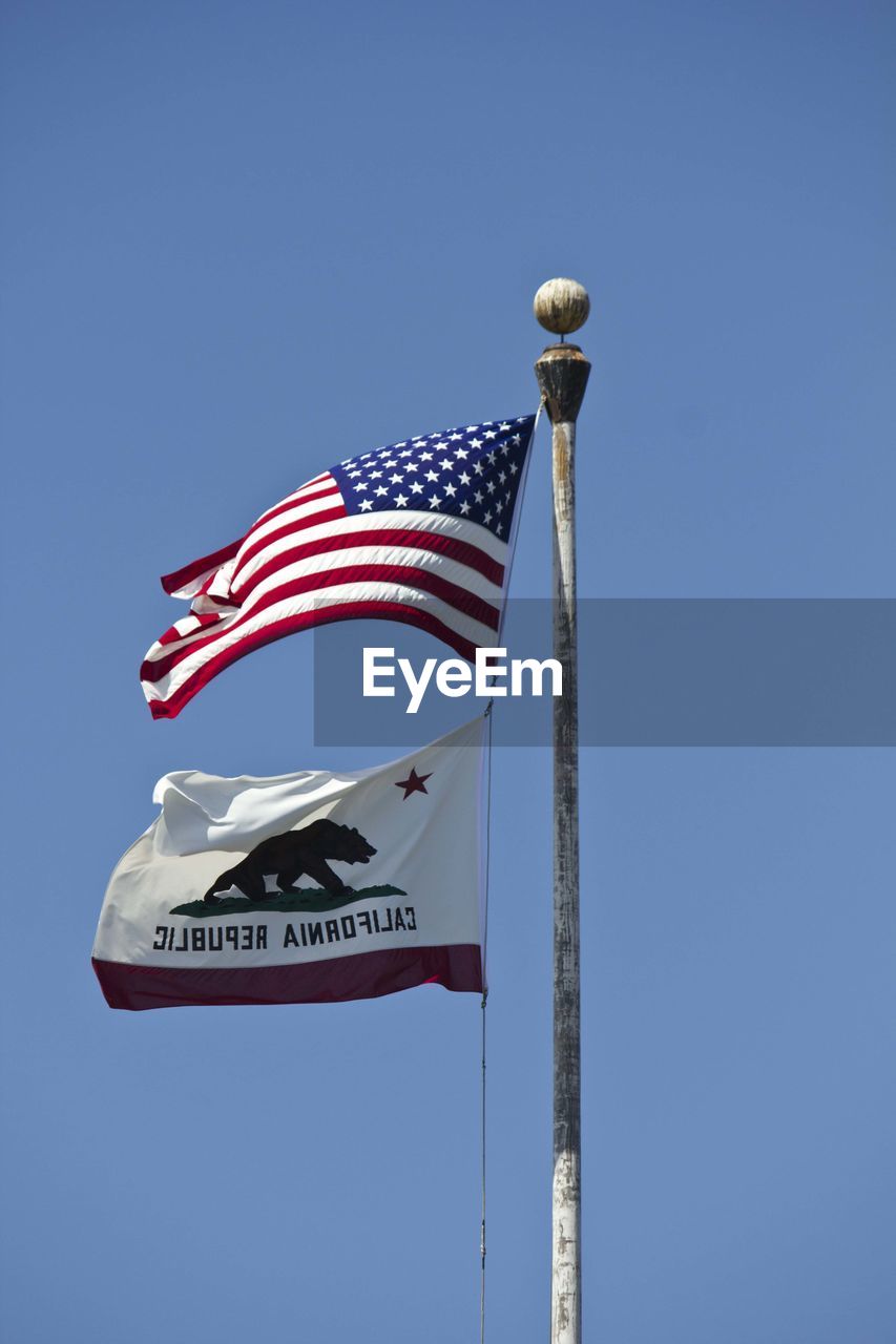 Low angle view of flags against clear blue sky