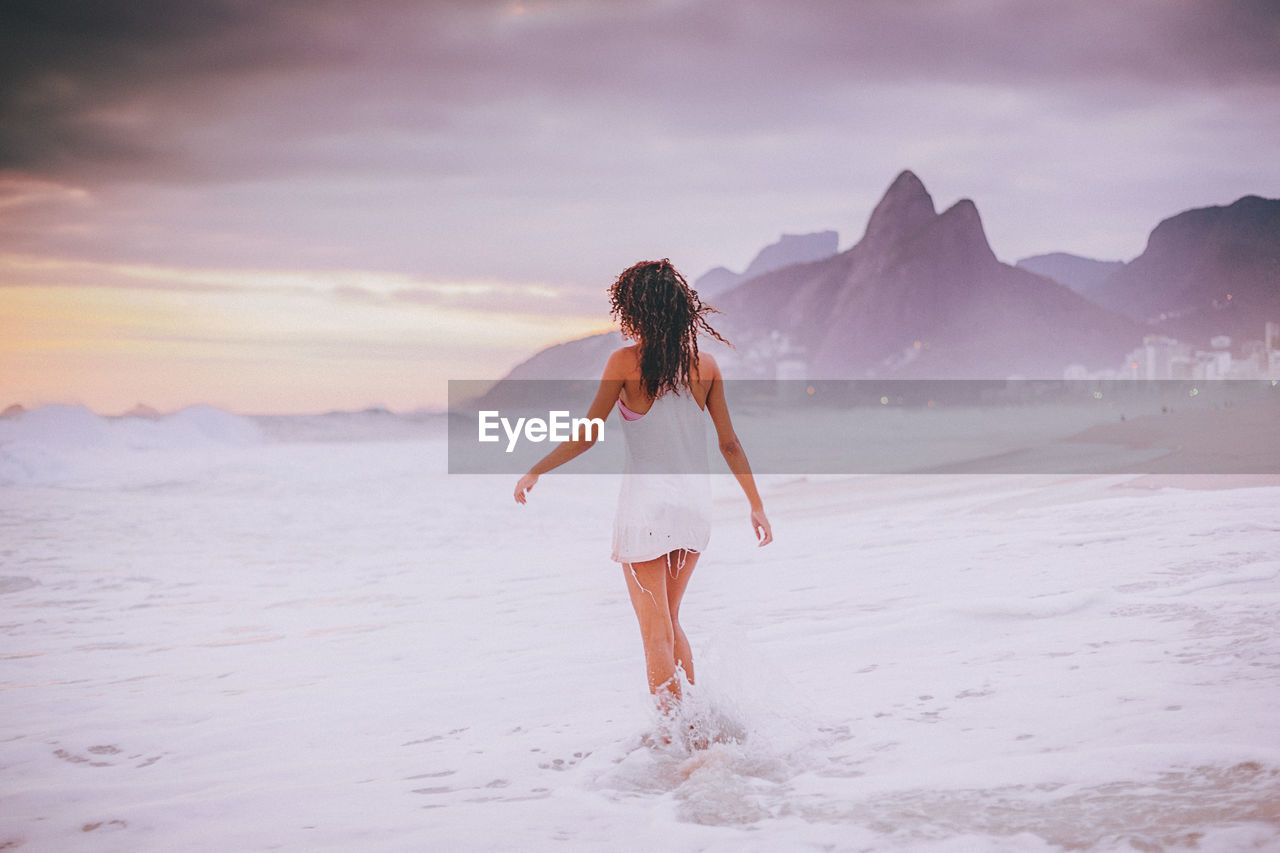 Rear view of woman walking on shore during sunset