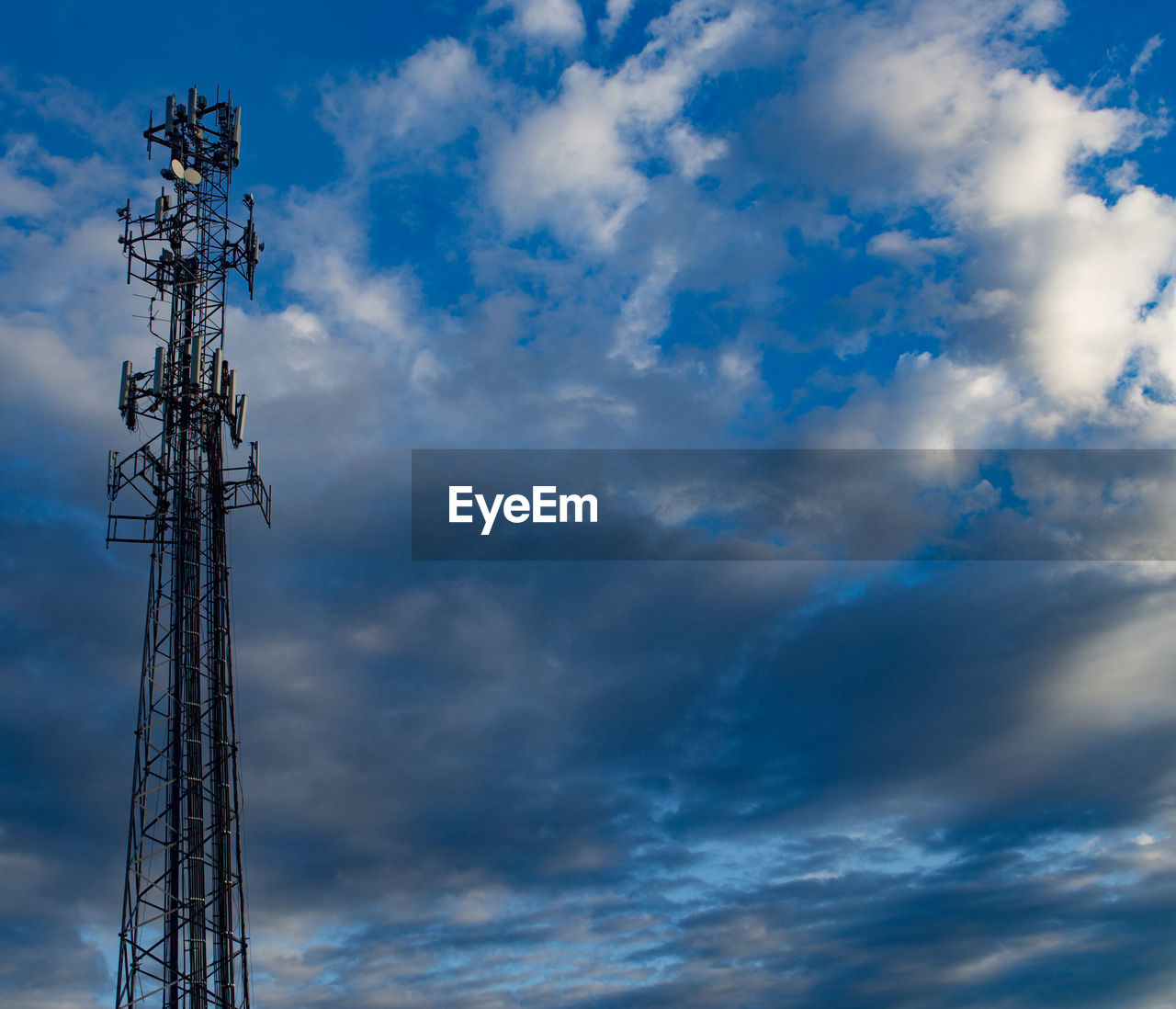 Low angle view of communications tower against cloudy sky