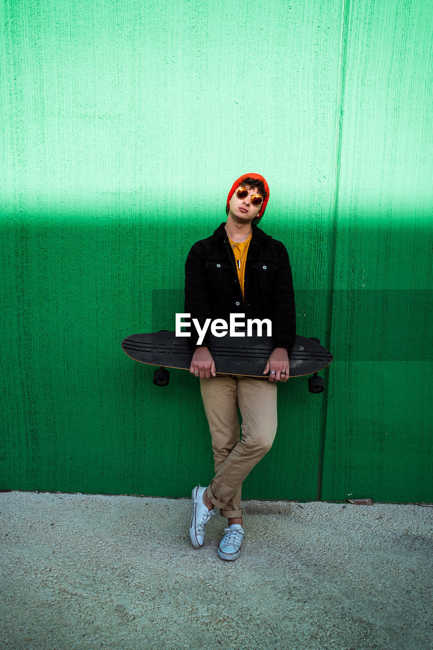 FULL LENGTH OF A YOUNG MAN SITTING ON WALL