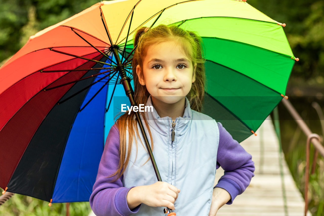 A girl holds a colorful umbrella while walking in the park.