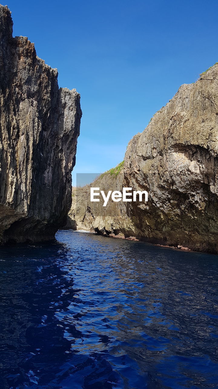 Rock formations in sea against clear blue sky