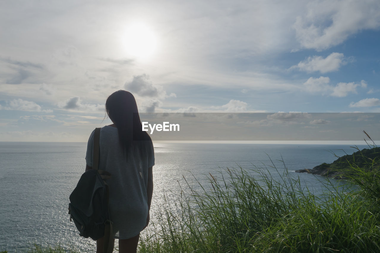 REAR VIEW OF MAN LOOKING AT SEA SHORE AGAINST SKY