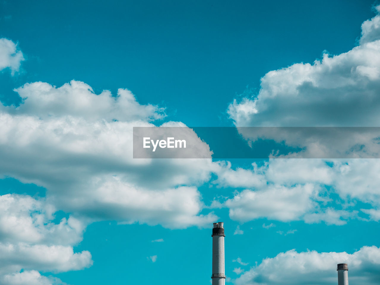 Low angle view of two chimneys against cloudy sky