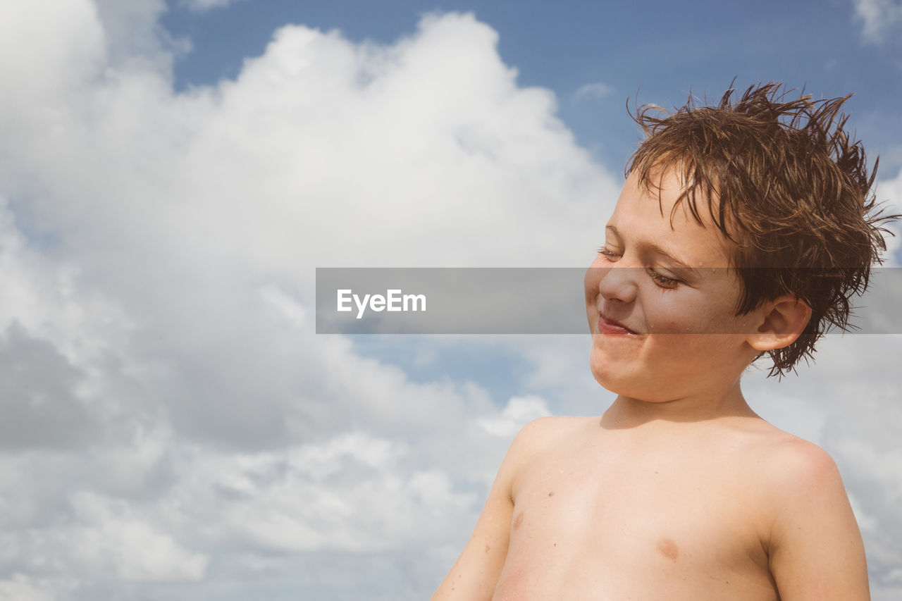 Smiling shirtless boy against sky