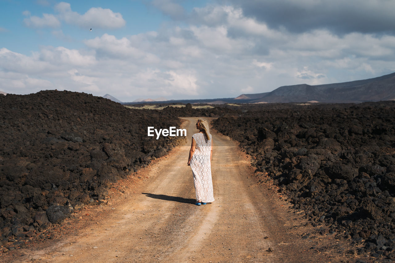 Rear view of woman standing on dirt road against sky