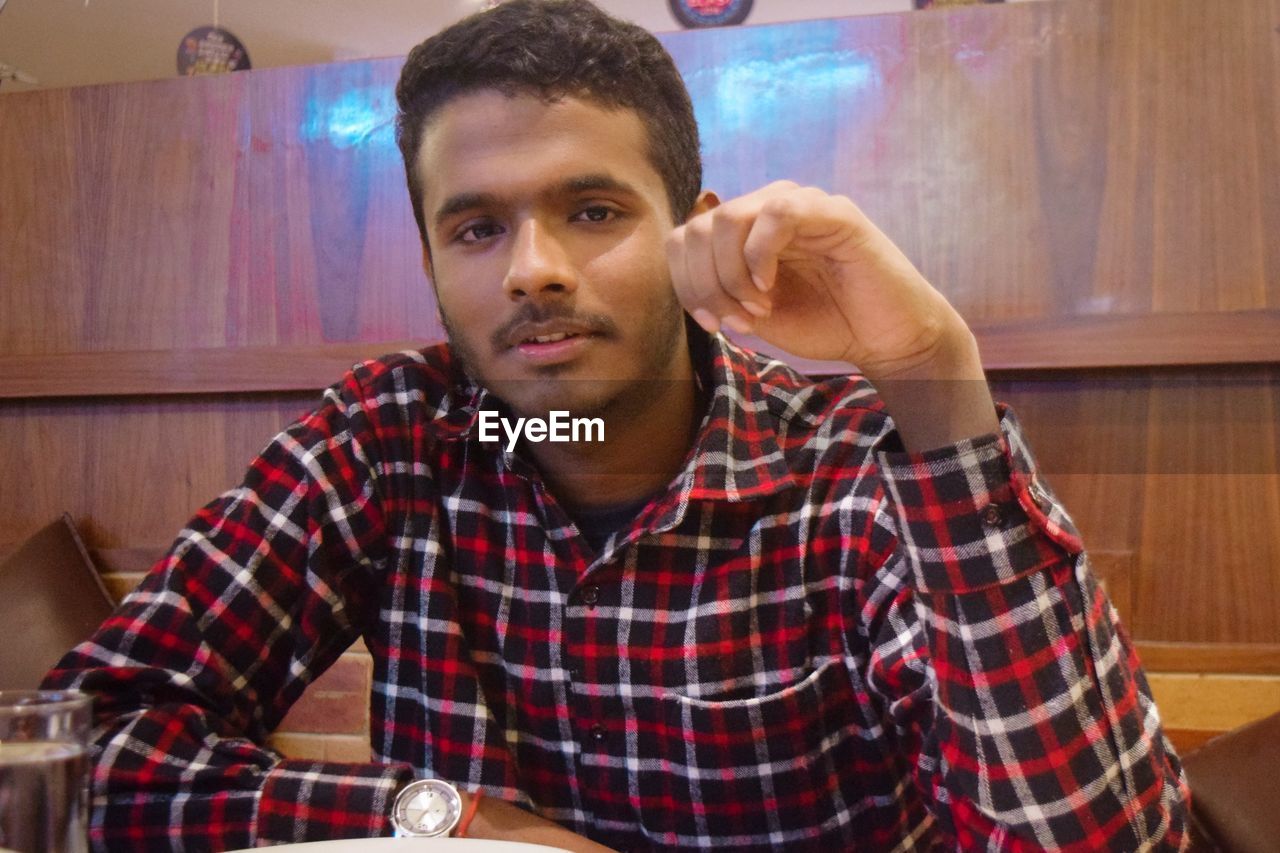 PORTRAIT OF YOUNG MAN SITTING AT RESTAURANT