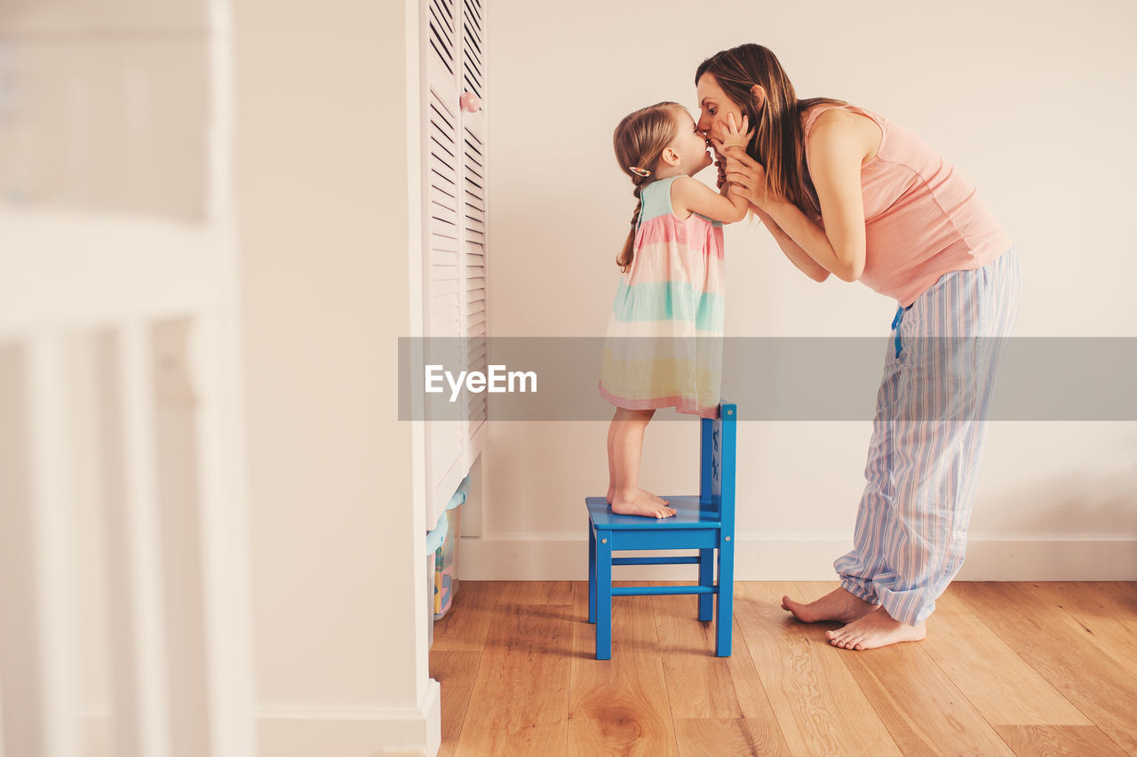 Mother kissing daughter on floor at home