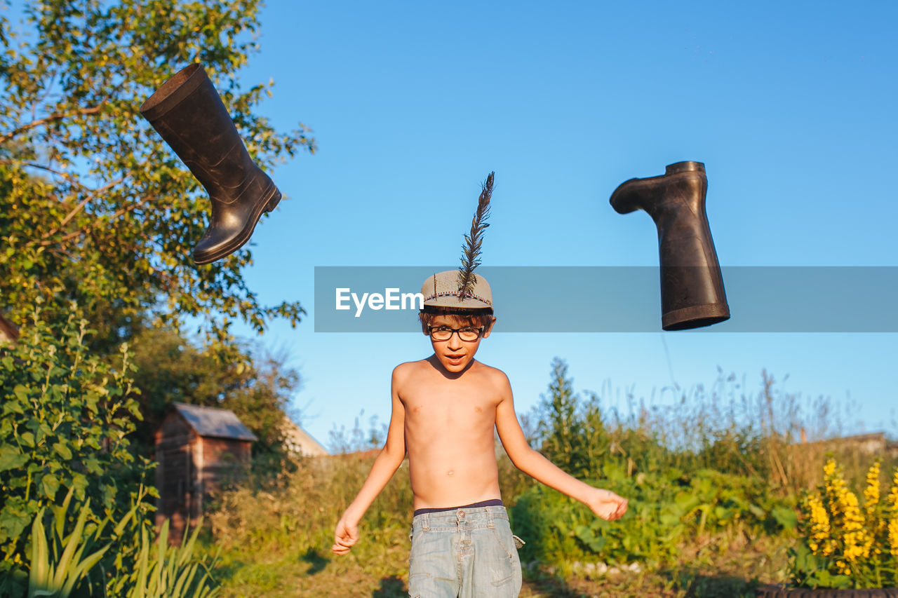 Shirtless boy with flying boots against sky