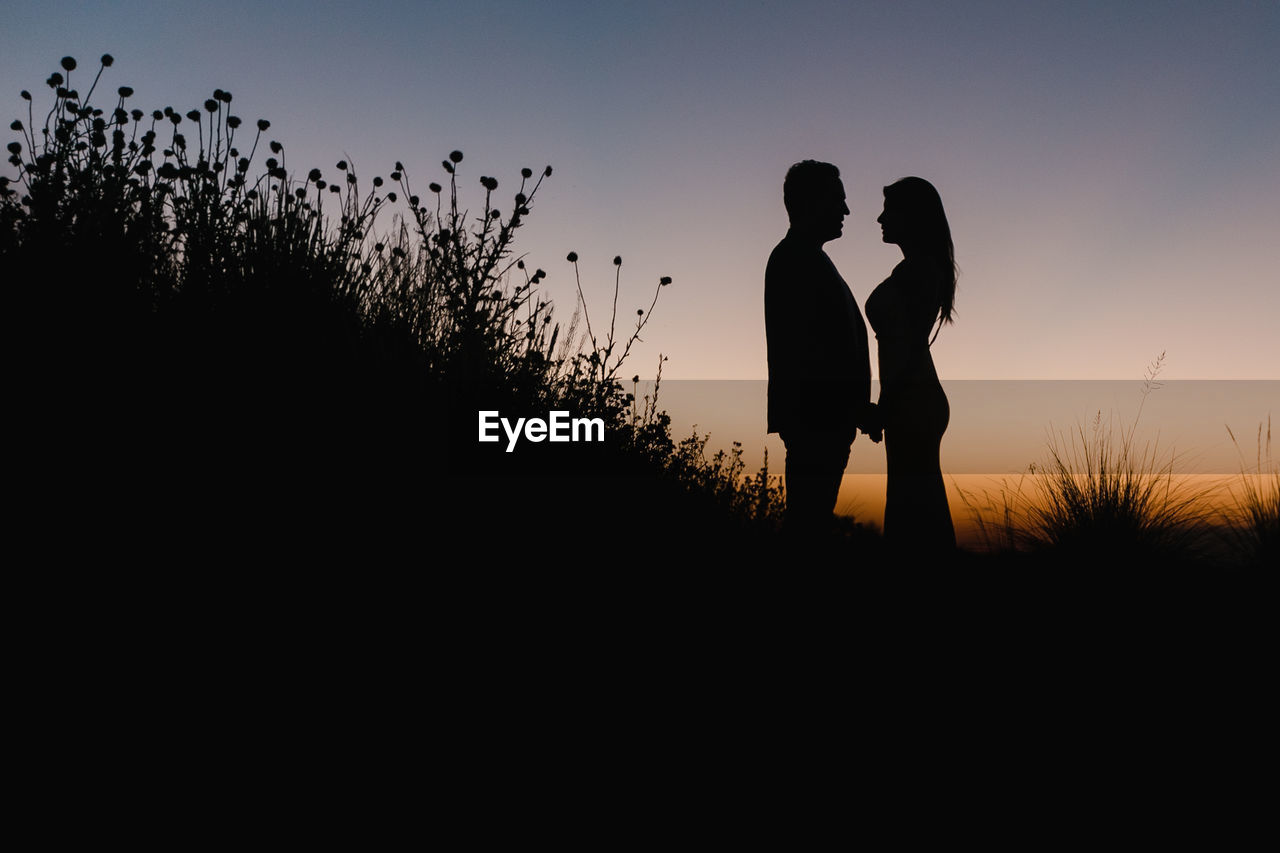 Silhouette of couple standing on field against clear sky during sunset