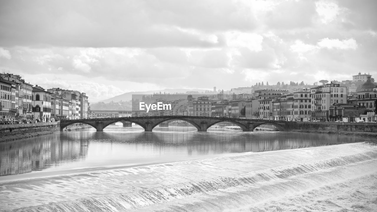 Bridge over river by buildings against sky