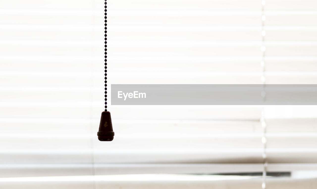 Close-up of string hanging against white blinds