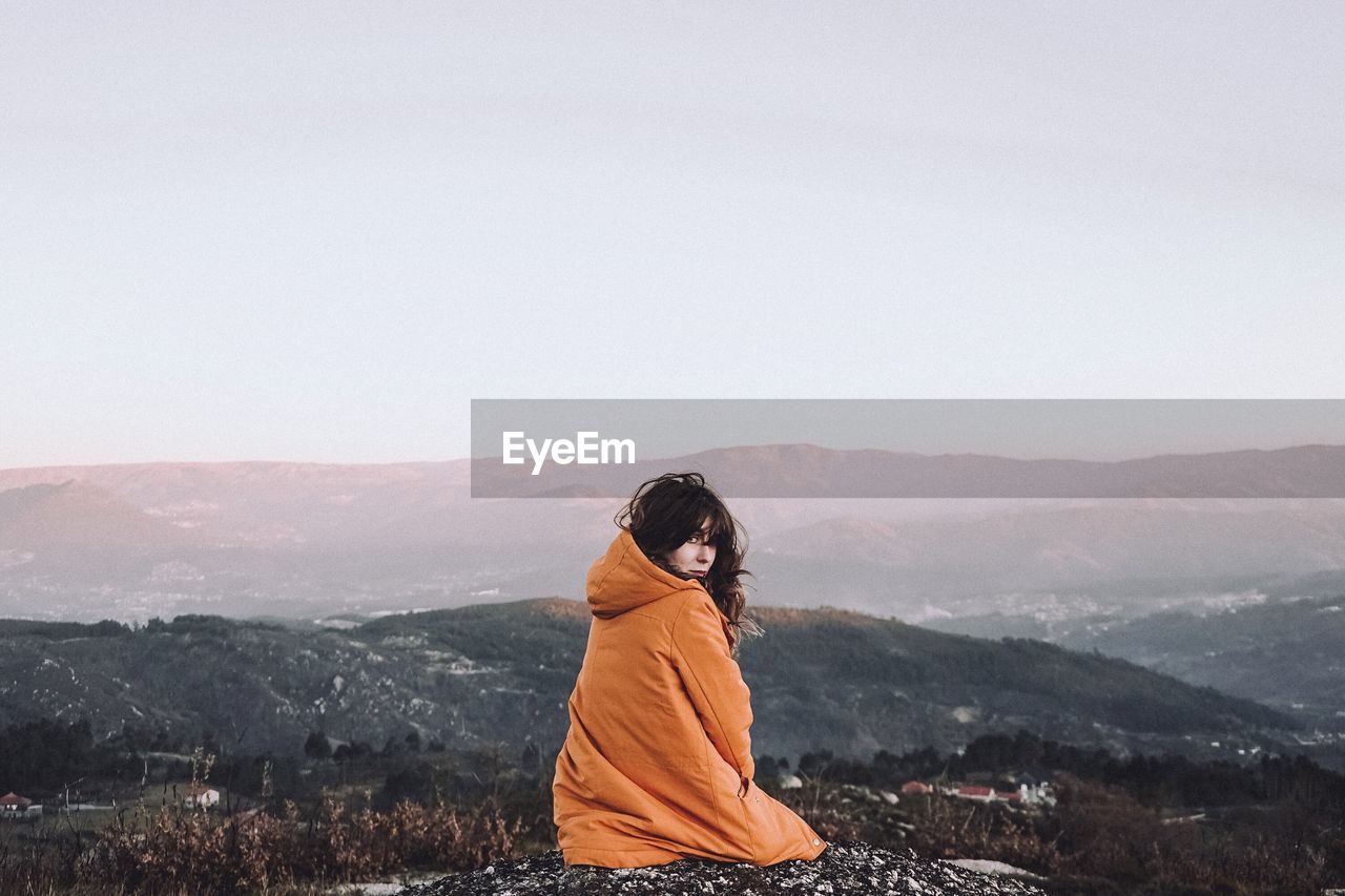 Woman sitting on mountain against sky