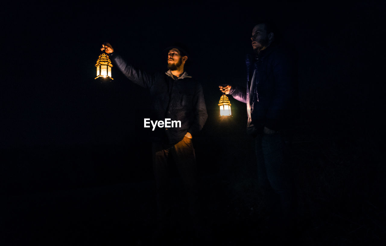 Friends holding illuminated lanterns while standing outdoors at night