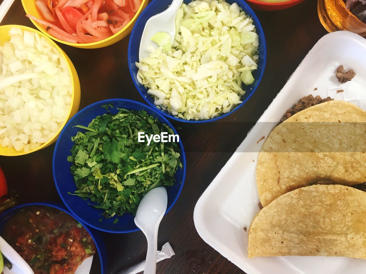 Directly above shot of tacos with chopped vegetables in bowl on table