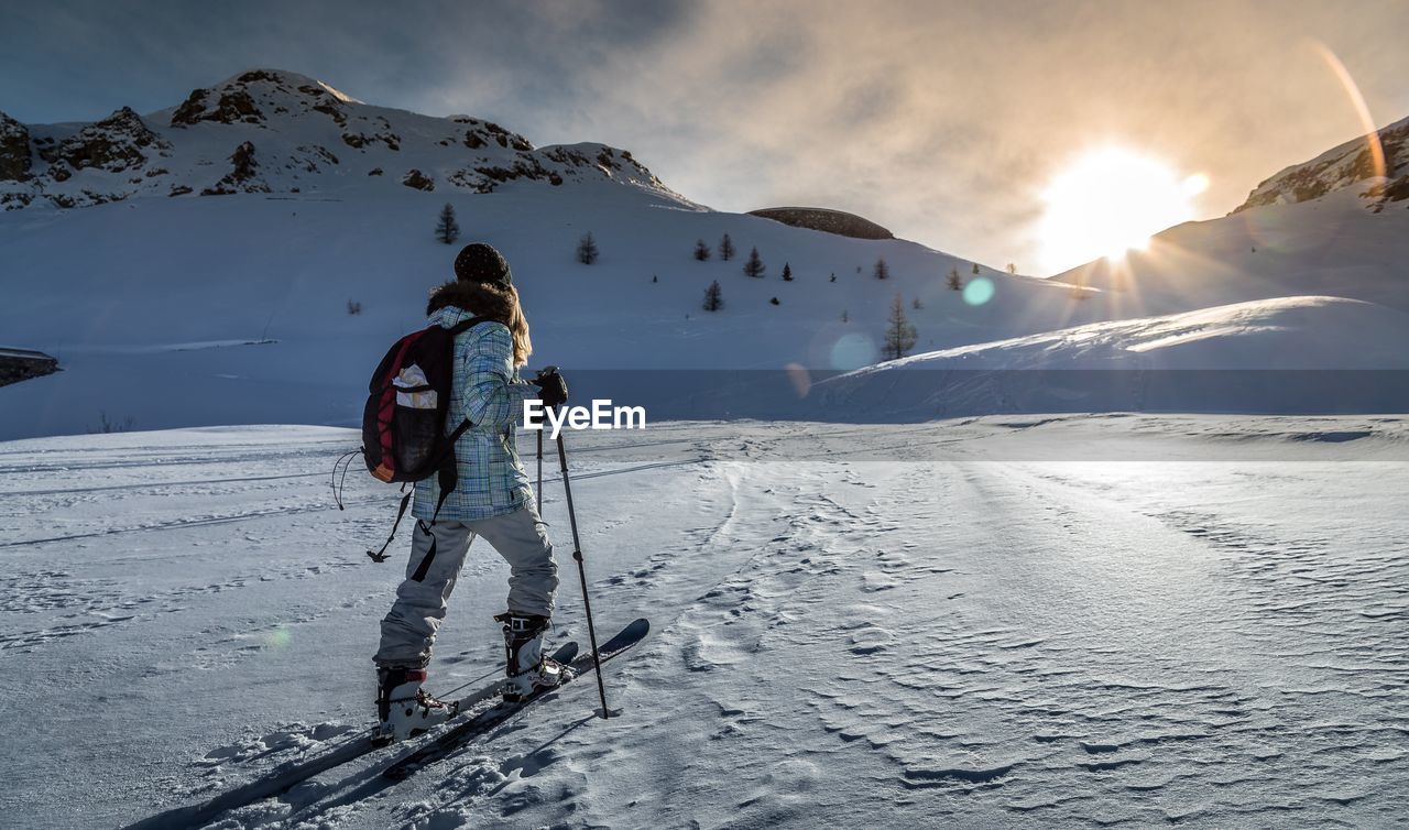 Girl skiing on snow covered landscape against sky during sunset