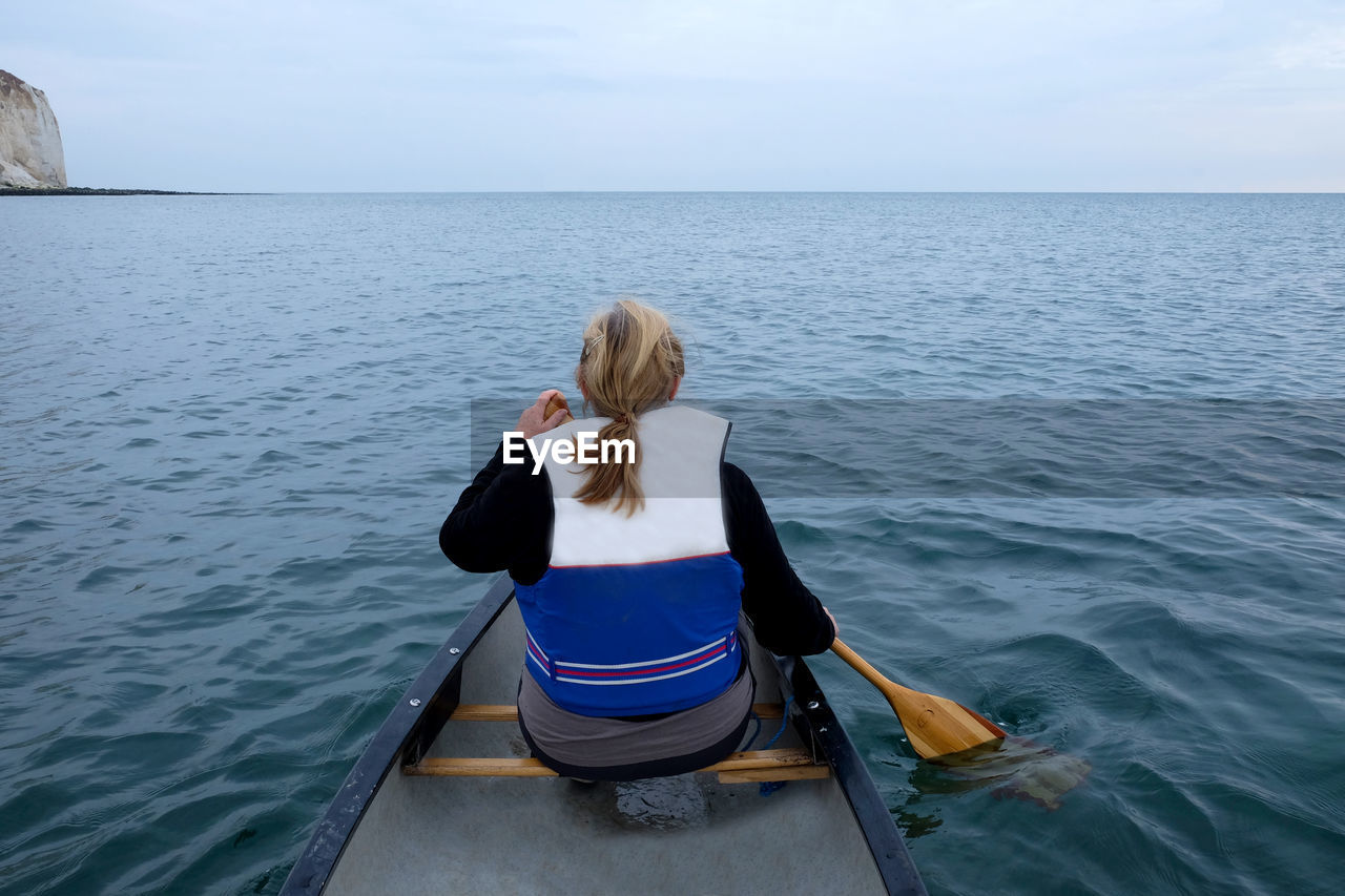 Rear view of woman rowing boat in sea against sky