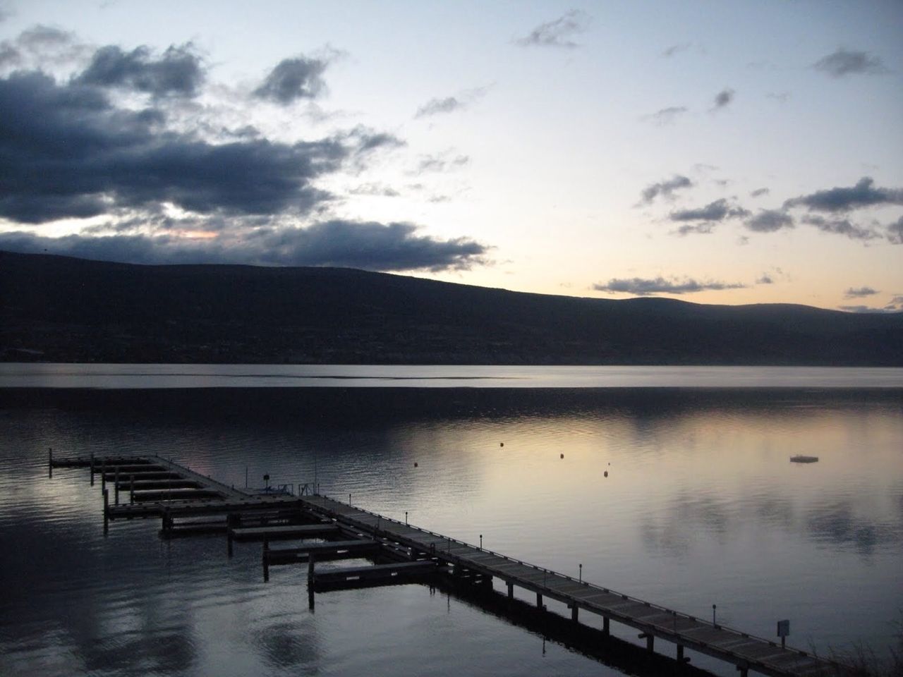 Pier on calm lake against silhouette mountain range