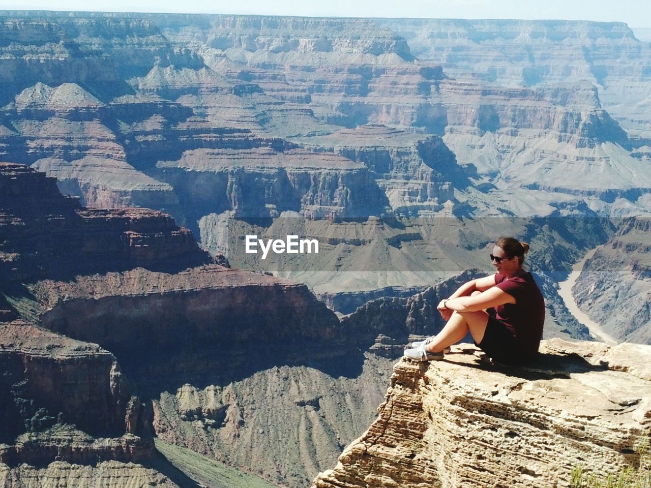 Full length of woman sitting on cliff against mountain