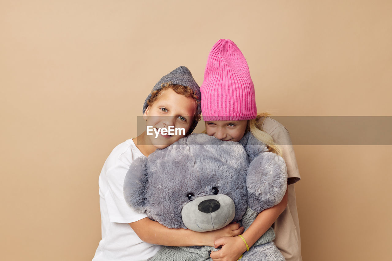 Cute sibling embracing stuffed toy against beige background