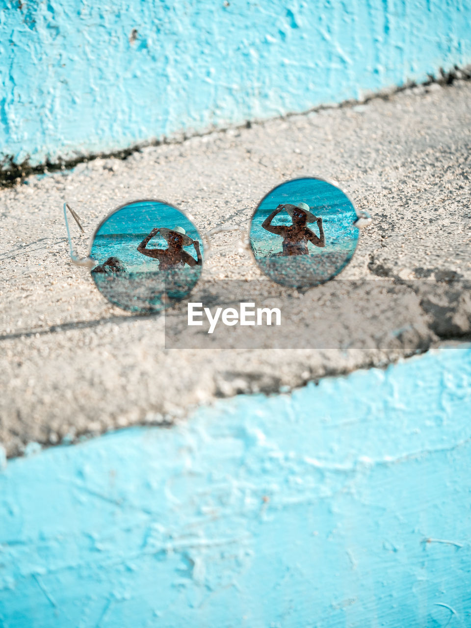 High angle view of sunglasses with reflection of woman wearing hat