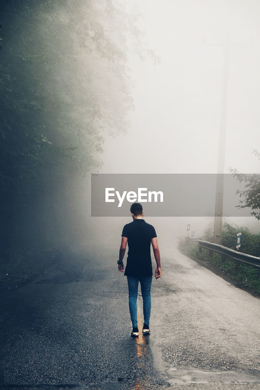 Full length rear view of man walking on wet road during rainy season