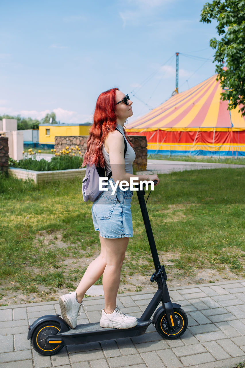 Young bright woman smiles and rides electric scooter in the summer in the city