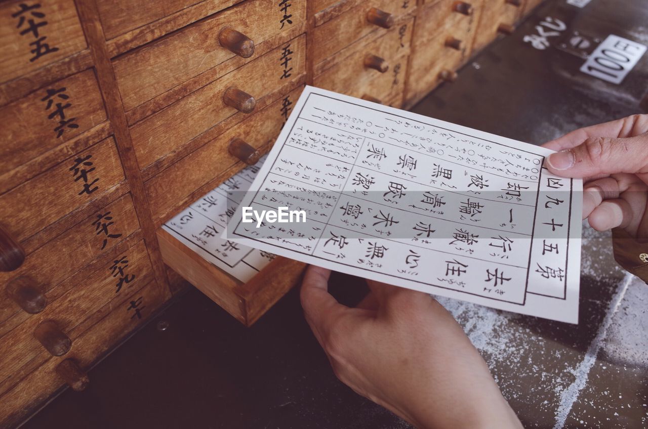 Cropped image of person holding fortune paper by wooden drawers