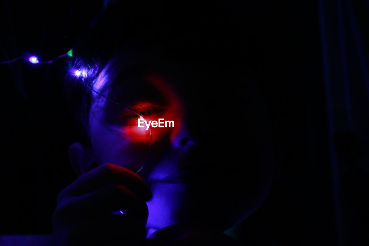 Close-up portrait of boy holding illuminated lighting equipment in darkroom