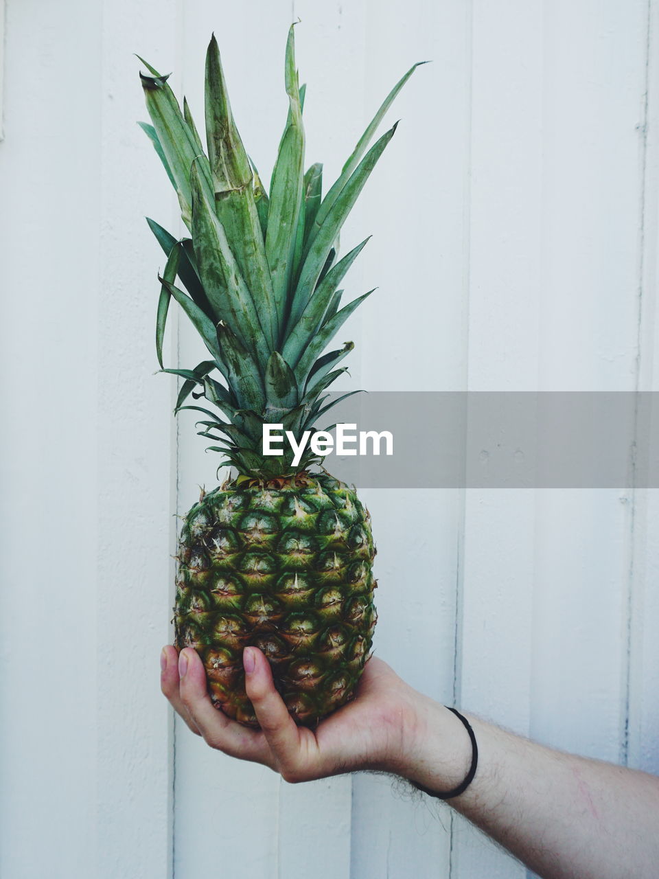 Cropped hand of person holding pineapple against wall