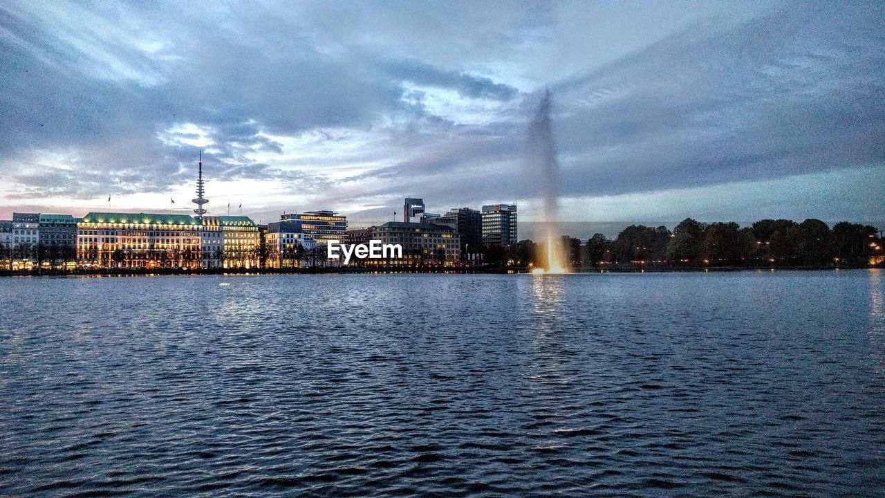 City at waterfront against cloudy sky