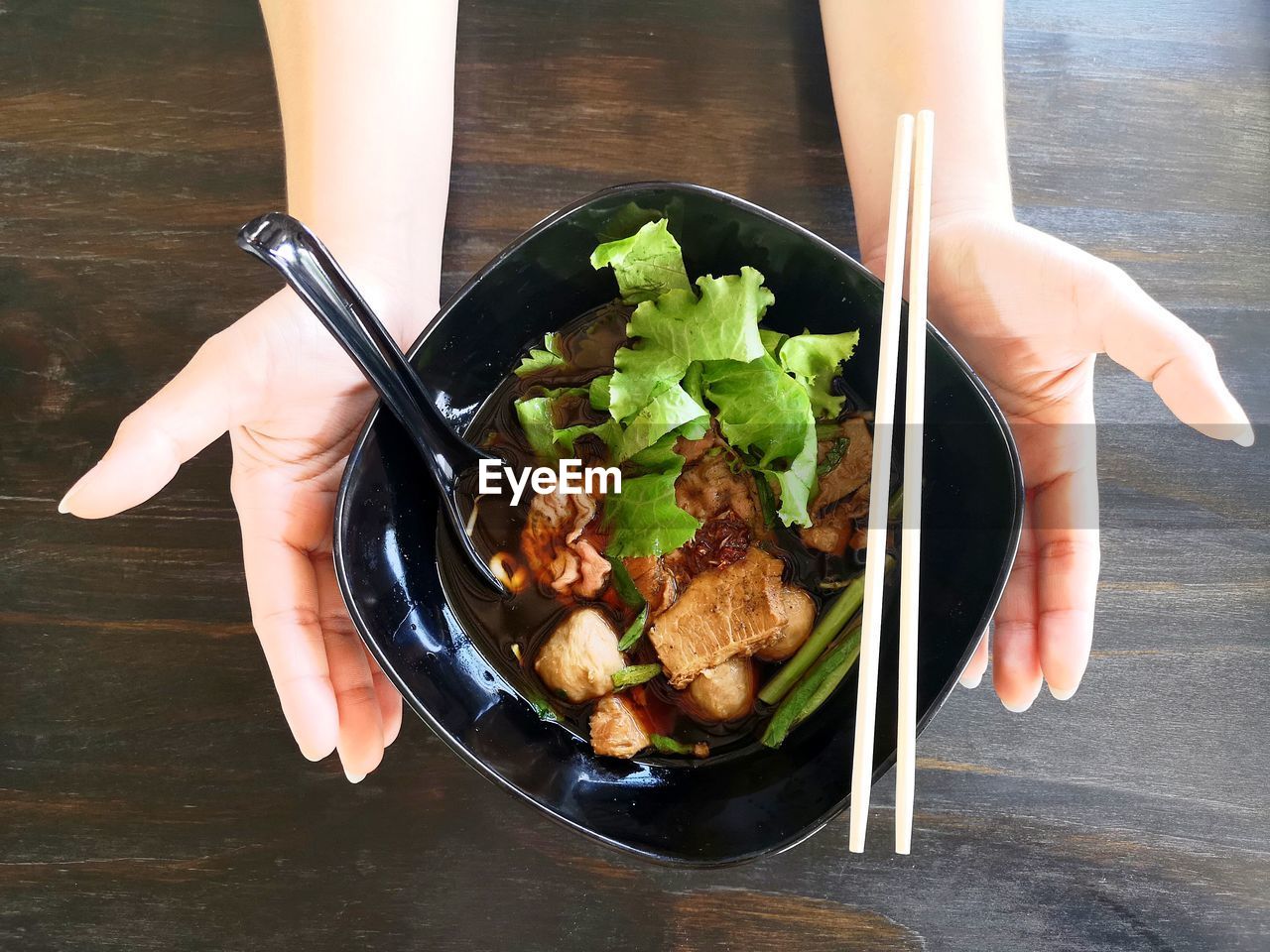 High angle view of two hand hold the black bowl of rice noodles soup with beef, meat ball