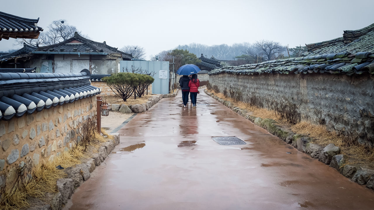 People walking on wet street on rainy day against sky