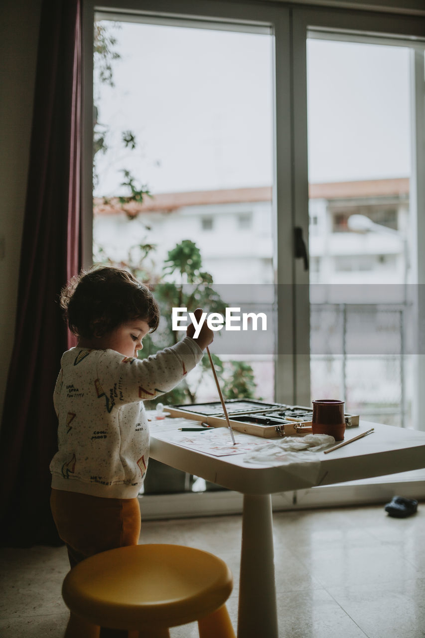 Side view of girl painting over paper on table at home