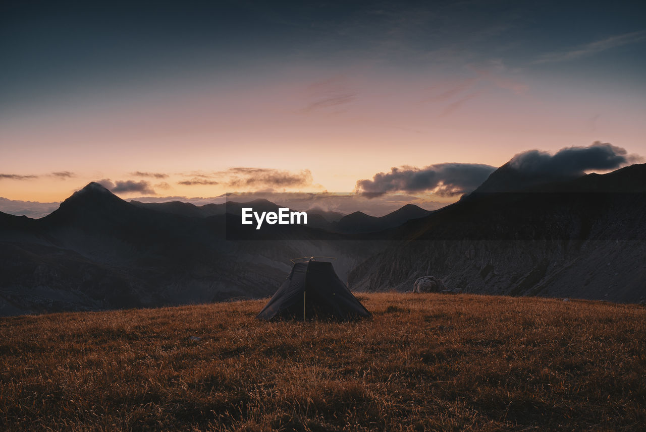 Tent on land with mountains in background against sky during sunrise