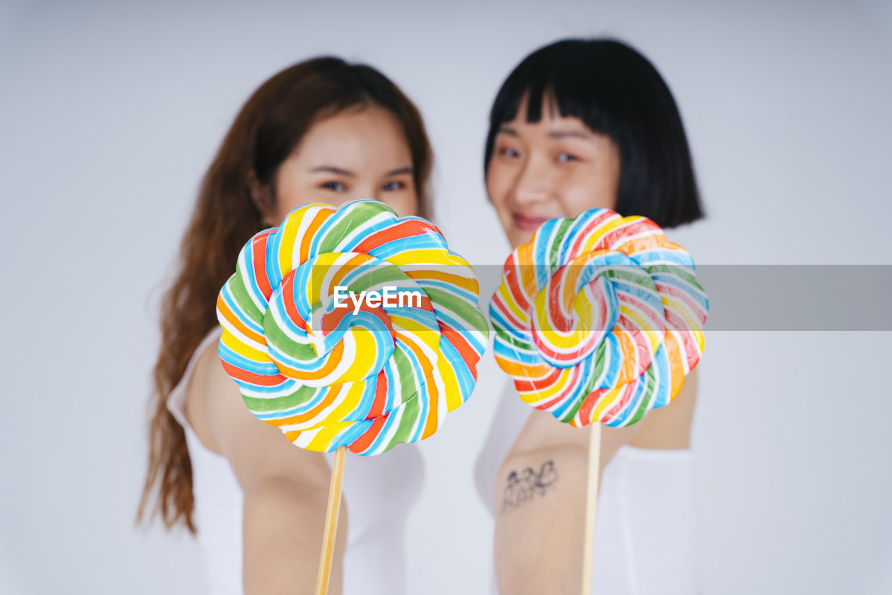 Portrait of lesbian couple holding lollipop against white background